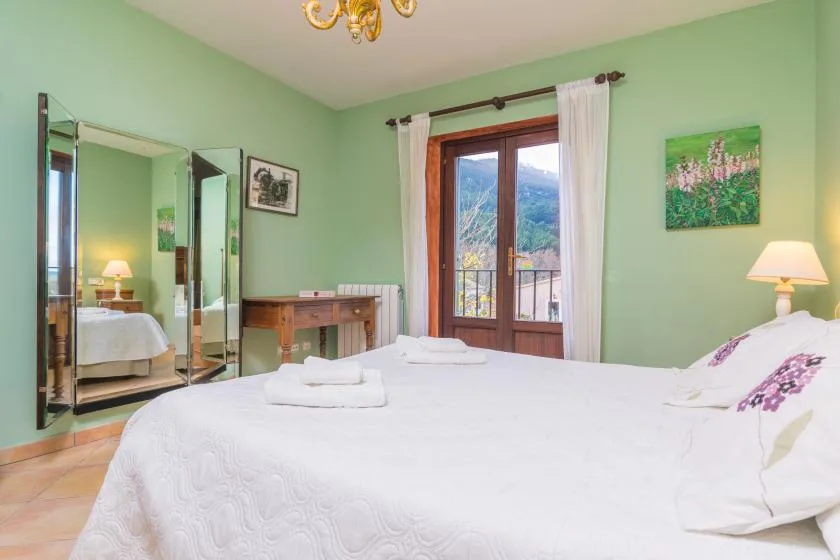 A bedroom with a large bed, mint-green walls, and a window overlooking greenery.
