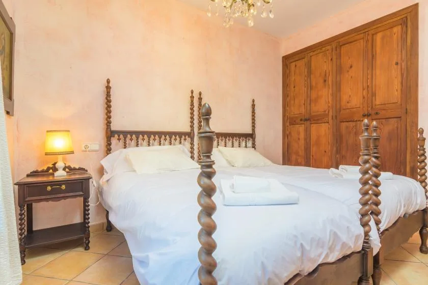 A bedroom with a white bed, dark wooden bedposts, and a large wooden wardrobe.