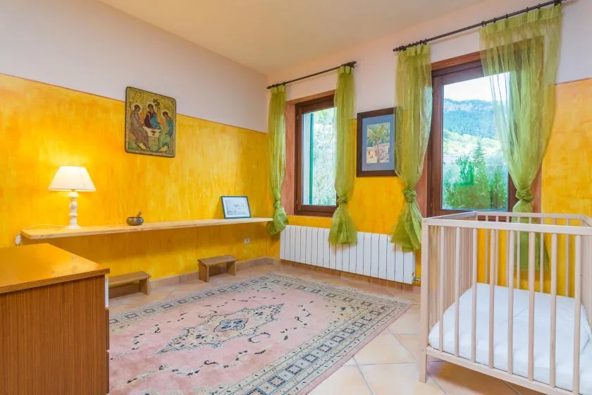 A bright room with yellow walls, green curtains, and a white crib beside the window.