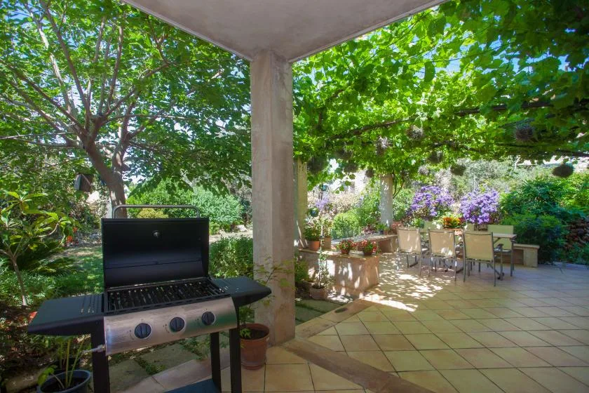 A covered patio overlooks a leafy garden, with outdoor seating and a grill.