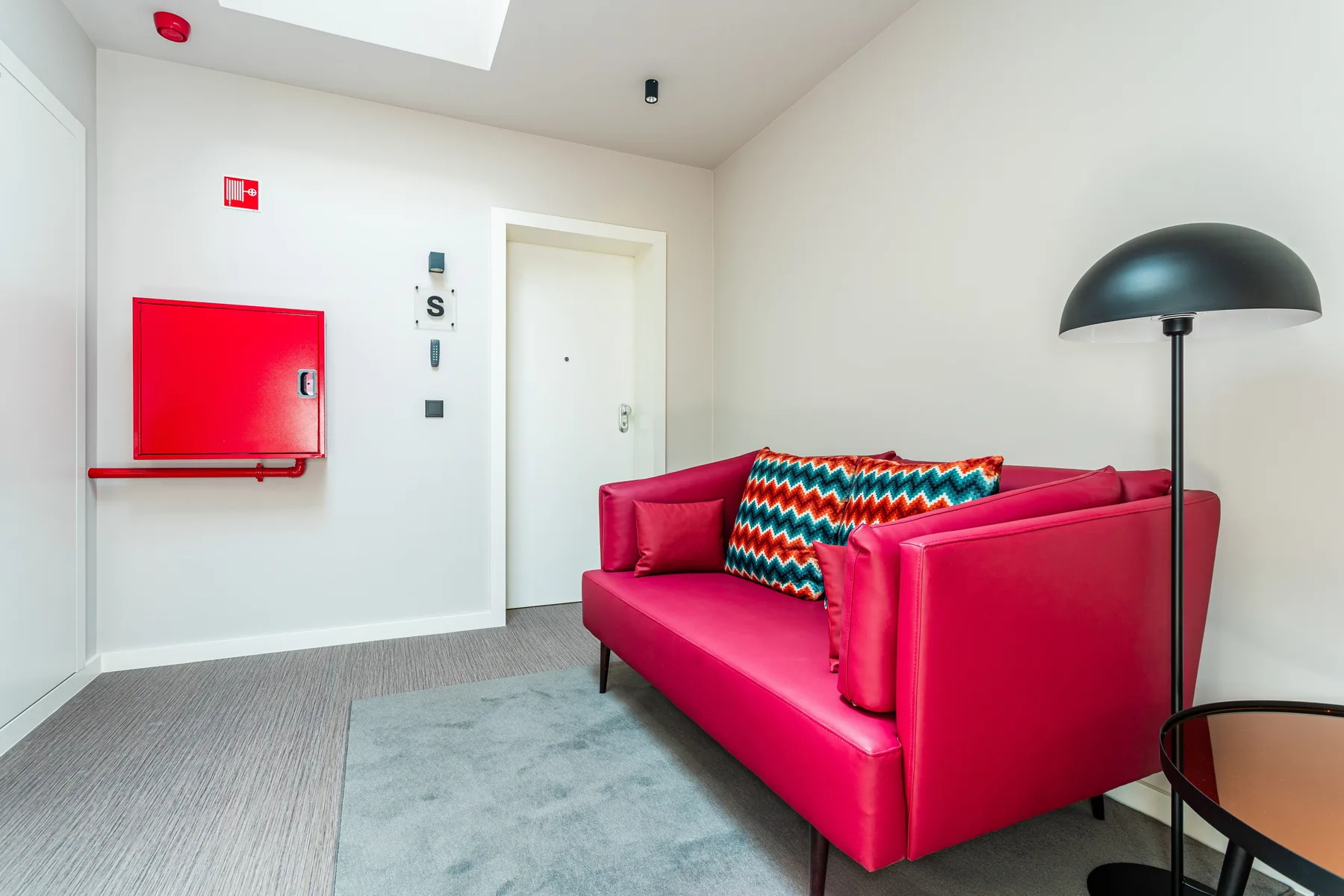 A bright living room with red seating, a patterned cushion, and a floor lamp.