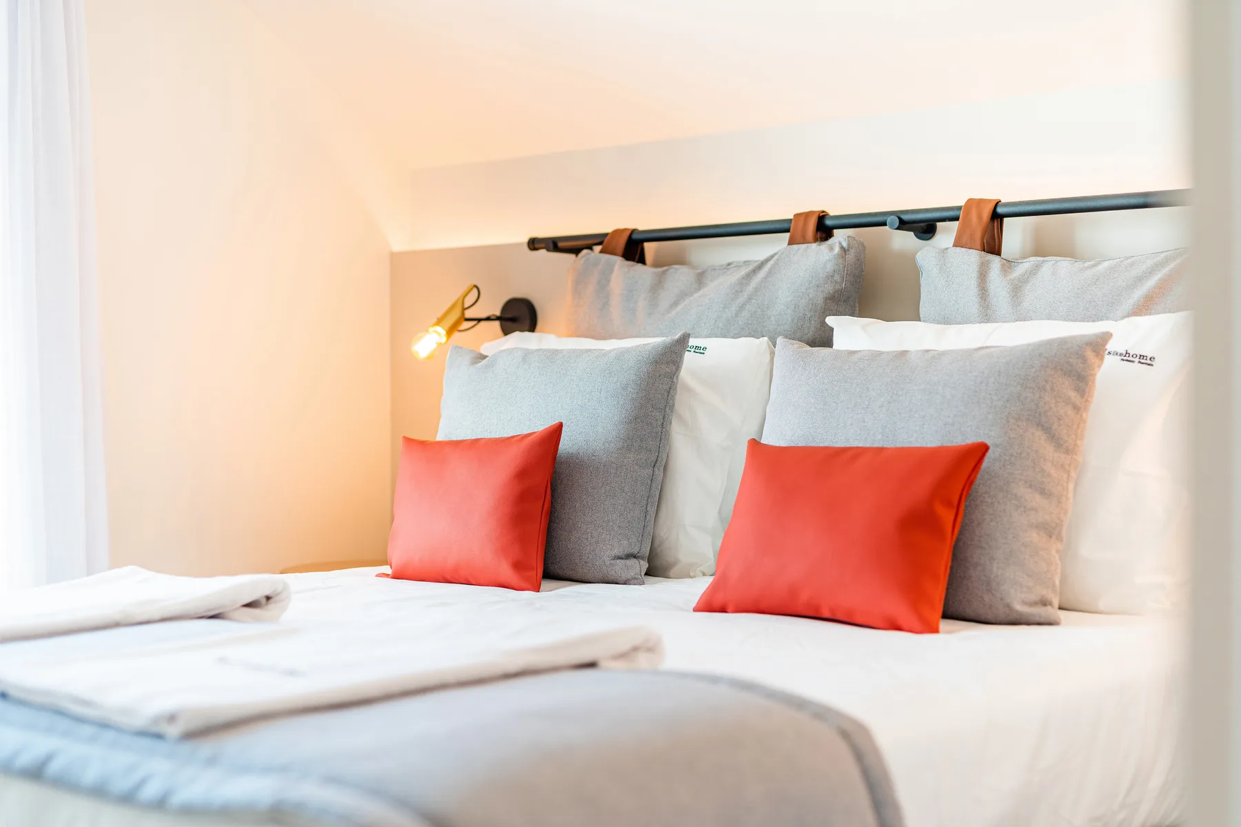 A bedroom with layered pillows and red accent cushions on the bed.