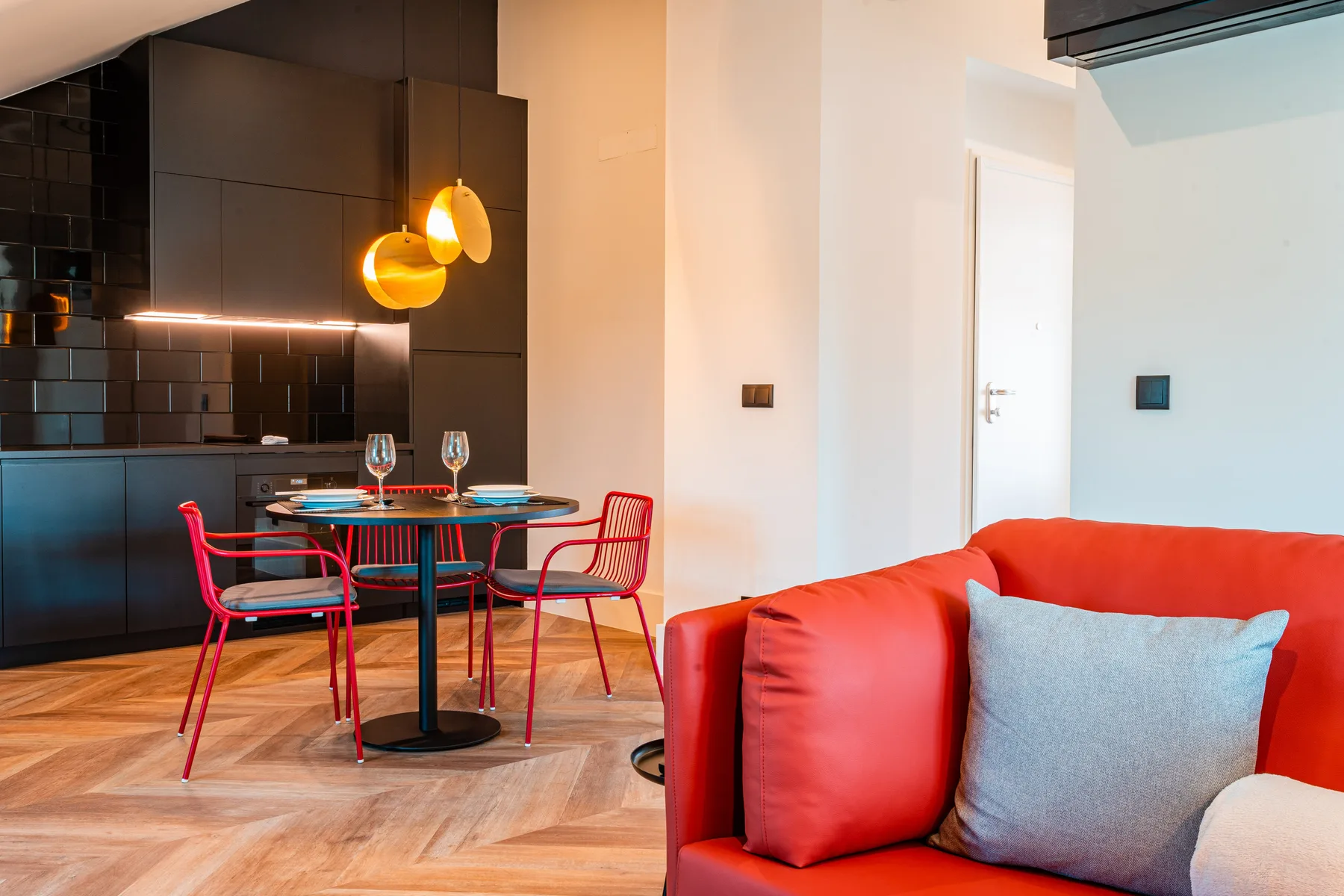 A living and dining area with red seating, a table, and a dark kitchen.