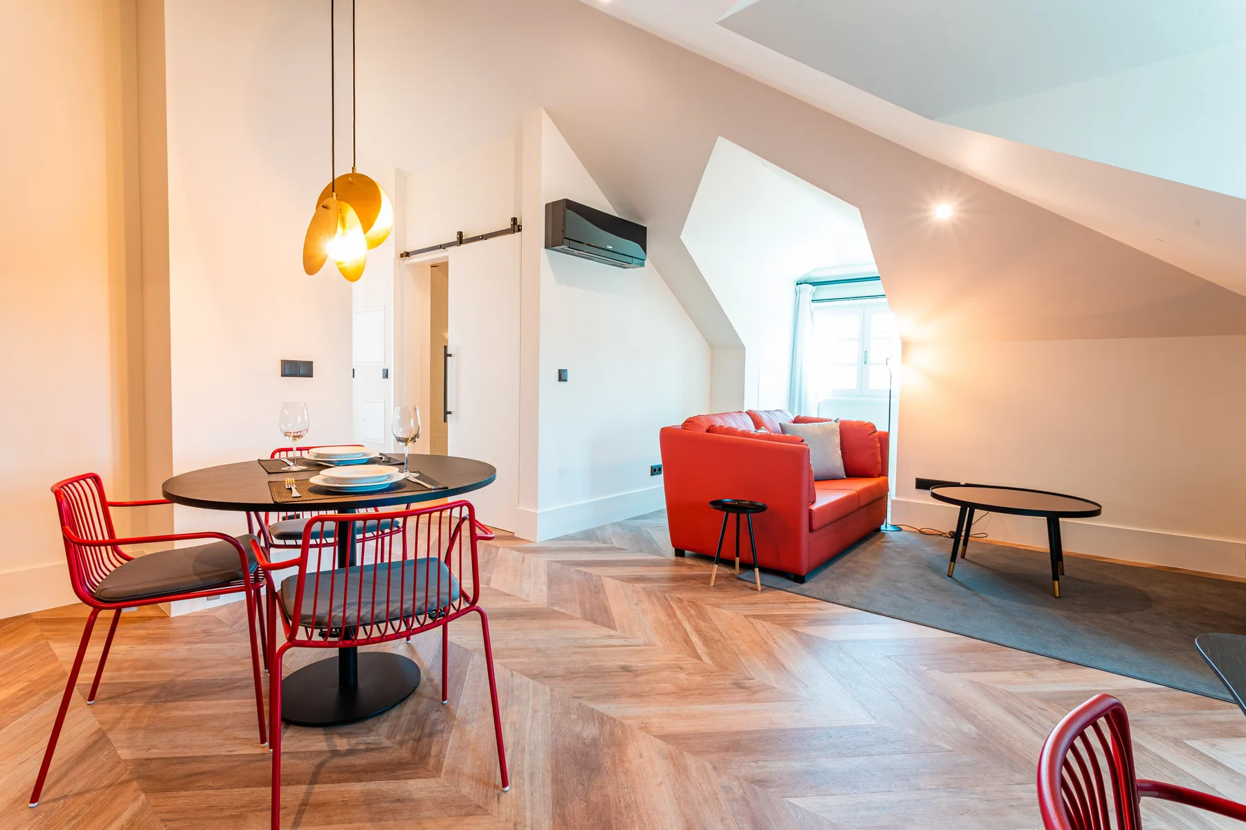 A dining and living area with a round table, red seating, and sloped ceilings.