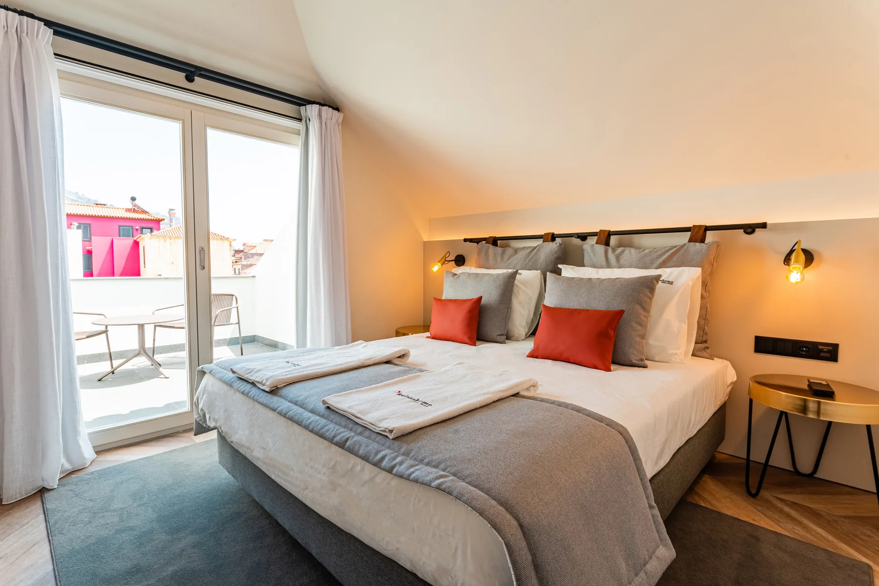 A bedroom with a neatly made bed beside glass doors opening onto a terrace.