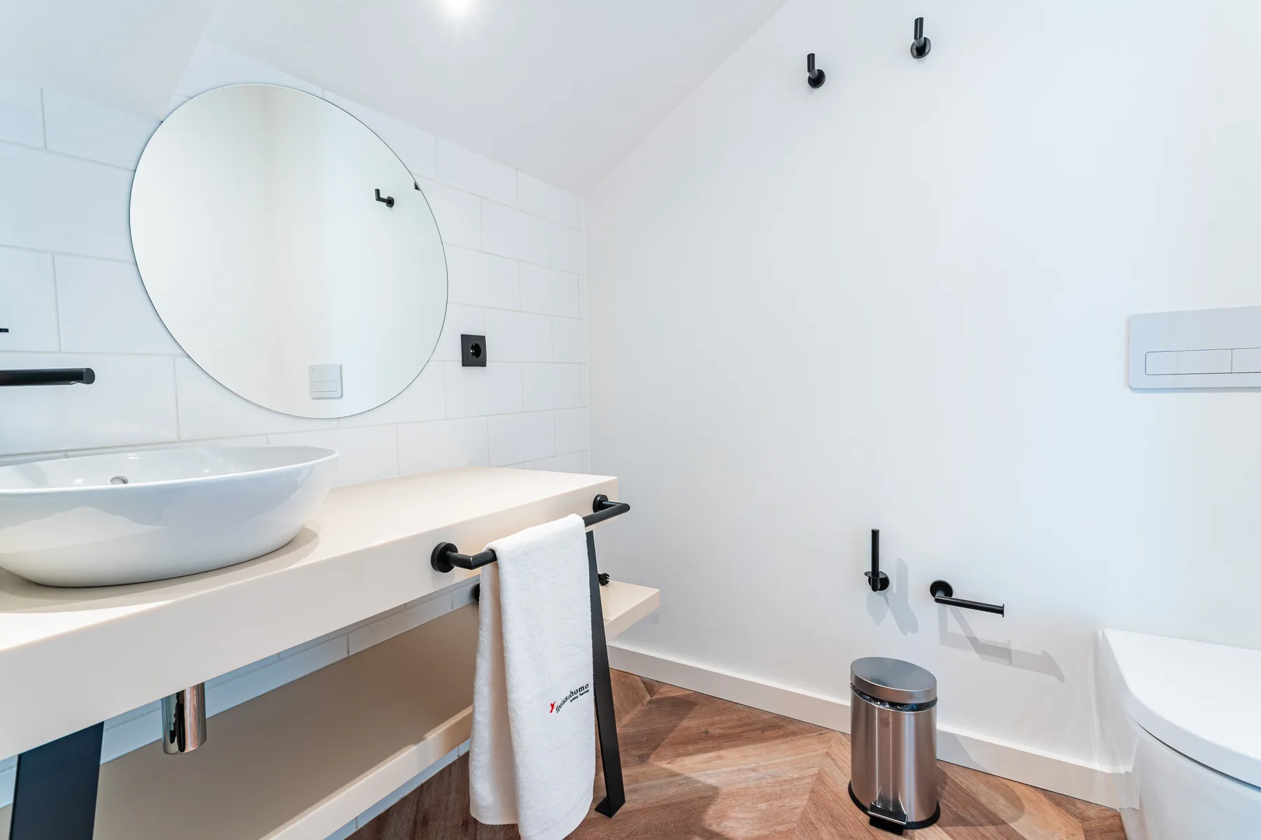 A bright bathroom with a round mirror, sink, and bathtub.