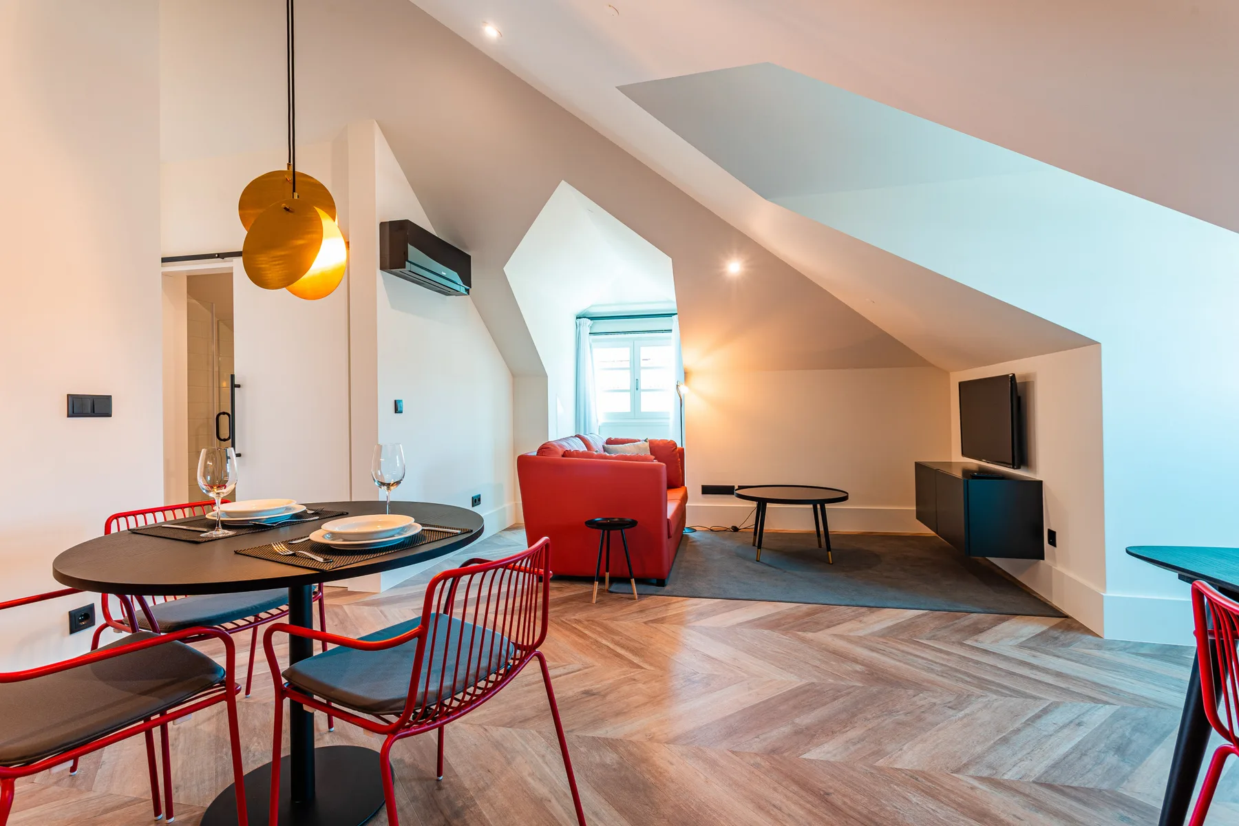 A bright attic living and dining area with red seating and a television.
