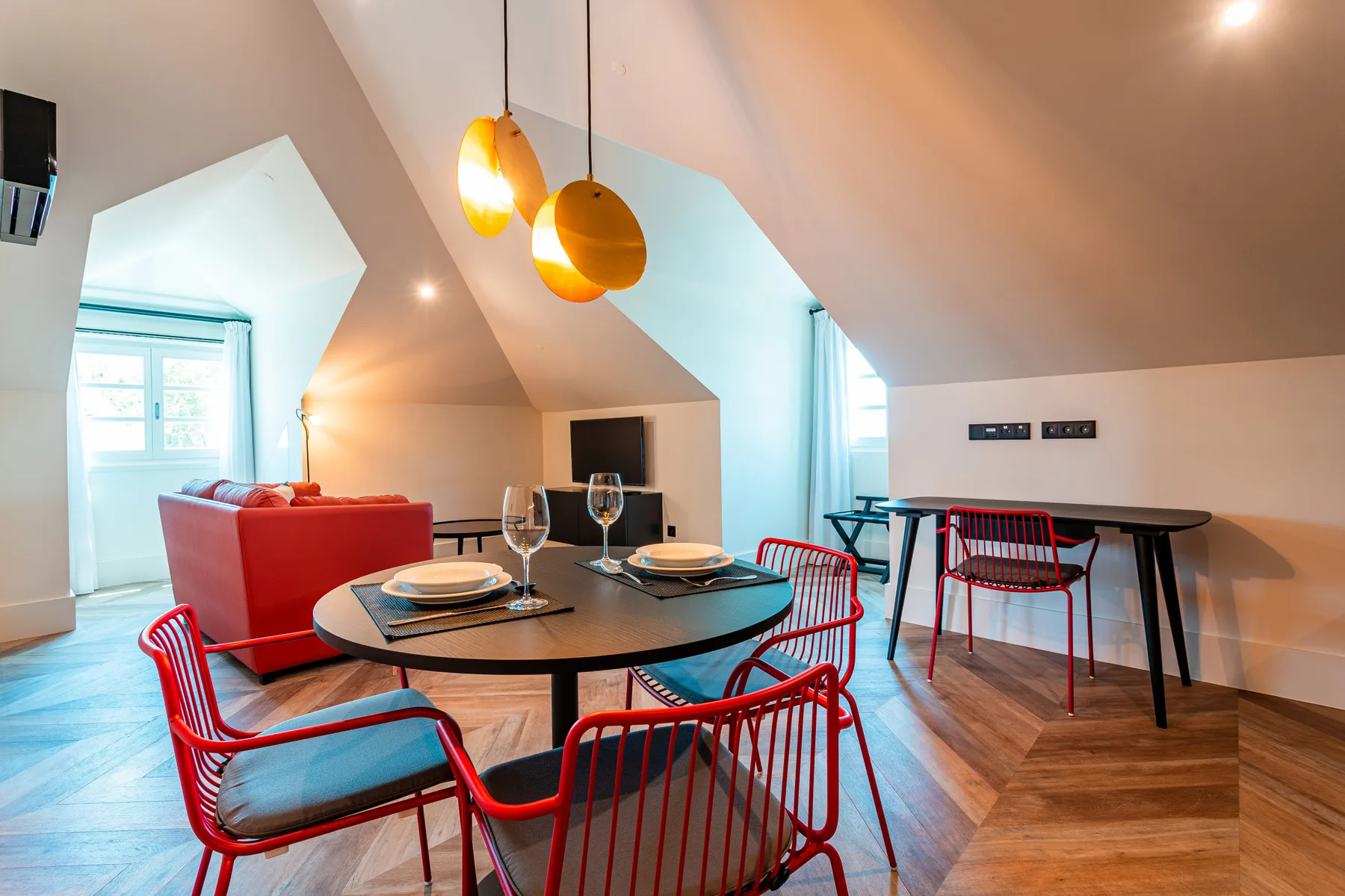A dining and living area with a round table, red seating, and pendant lights.