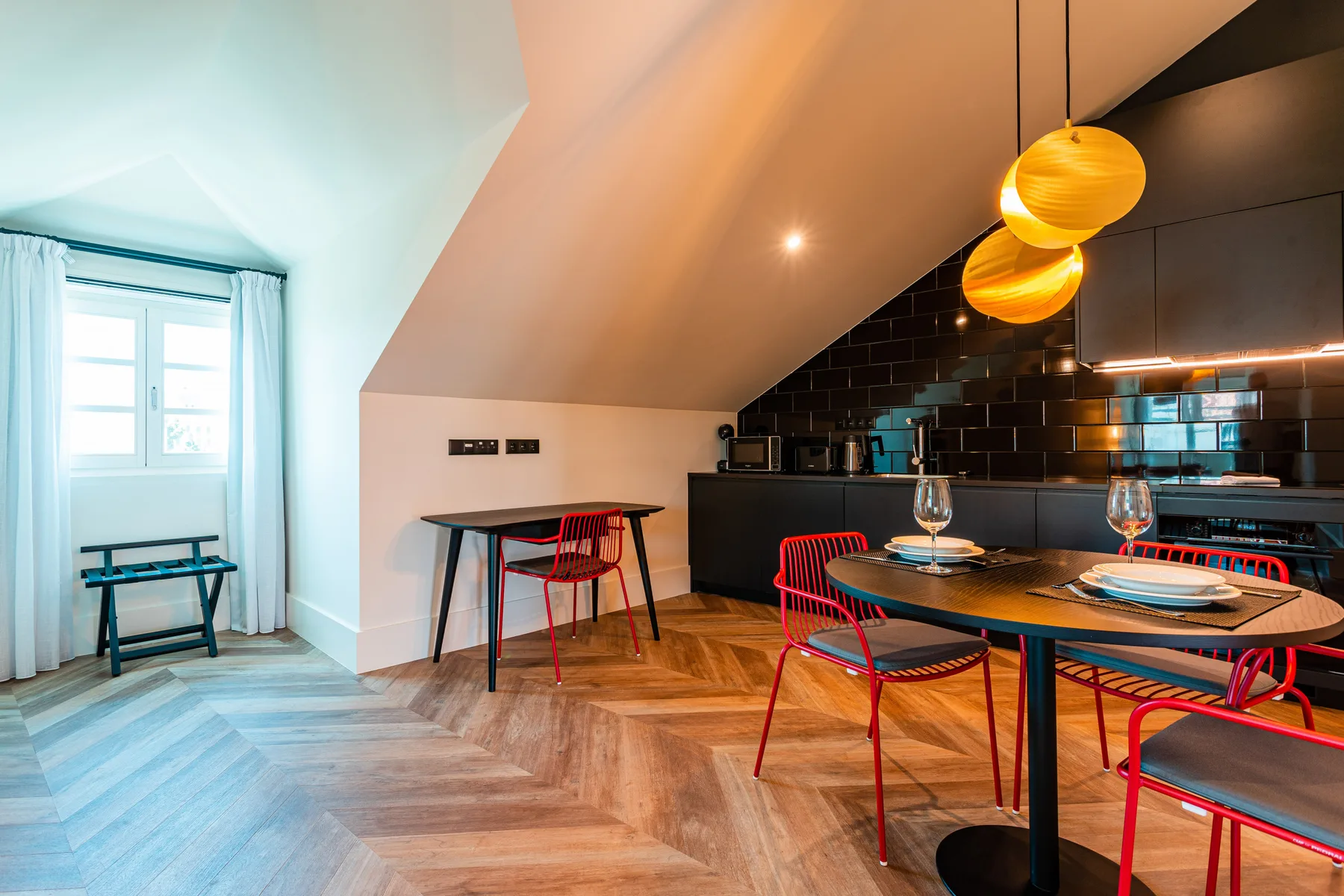 Dining area with a round table and red chairs beneath pendant lights.