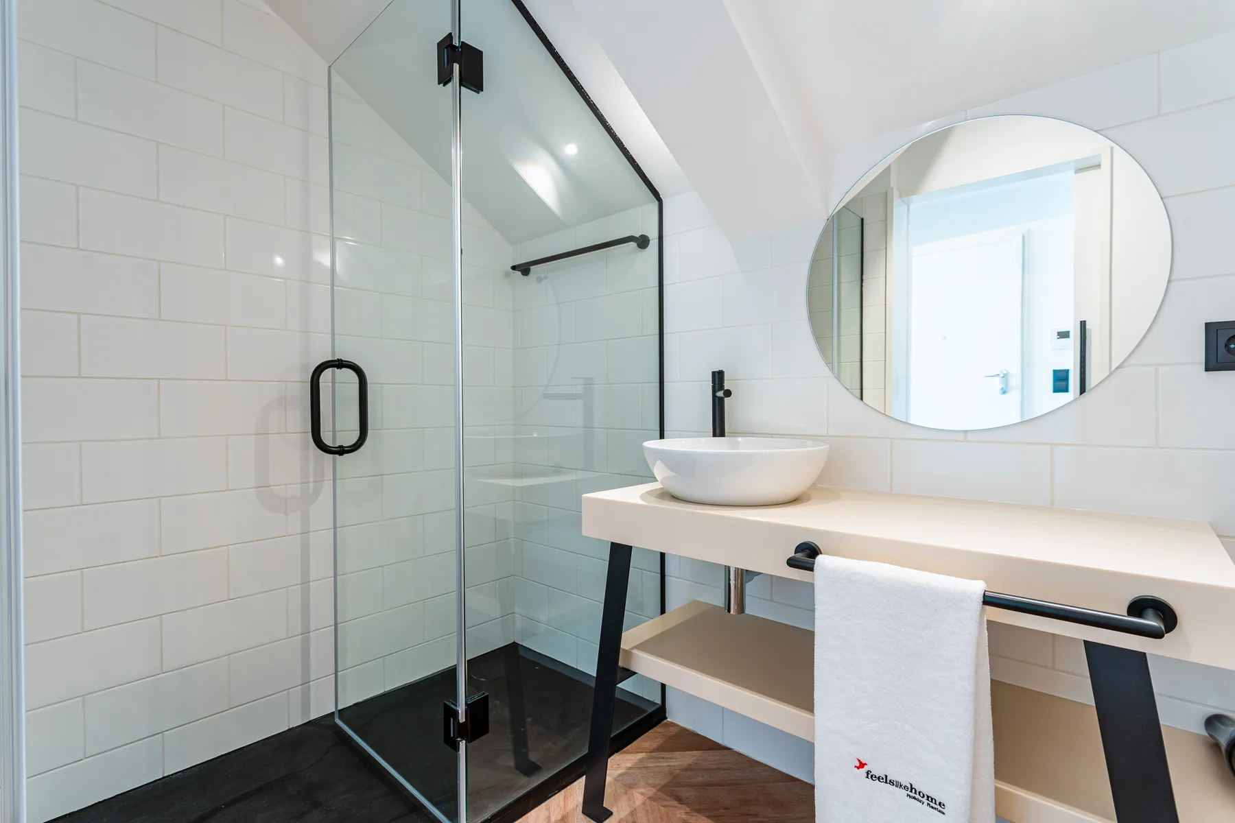 A modern bathroom with a glass shower and a round mirror above the sink.