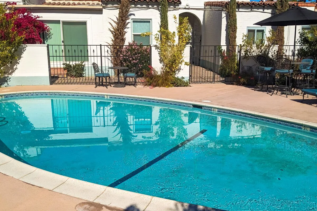 A swimming pool beside a patio with outdoor seating and a shaded umbrella.