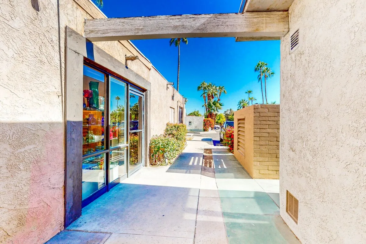A sunlit outdoor walkway runs between stucco walls, with glass doors on one side.