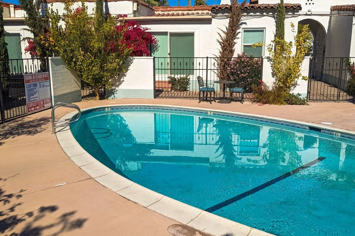 A swimming pool sits beside a white building and patio seating.