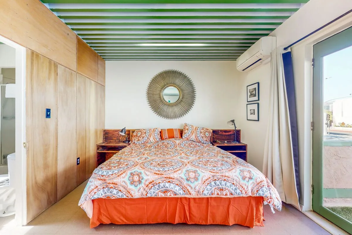 A bedroom with a patterned bedspread, wood cabinetry, and a glass door.