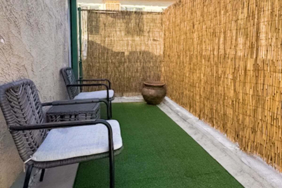 A small outdoor seating area with chairs beside a green artificial lawn.
