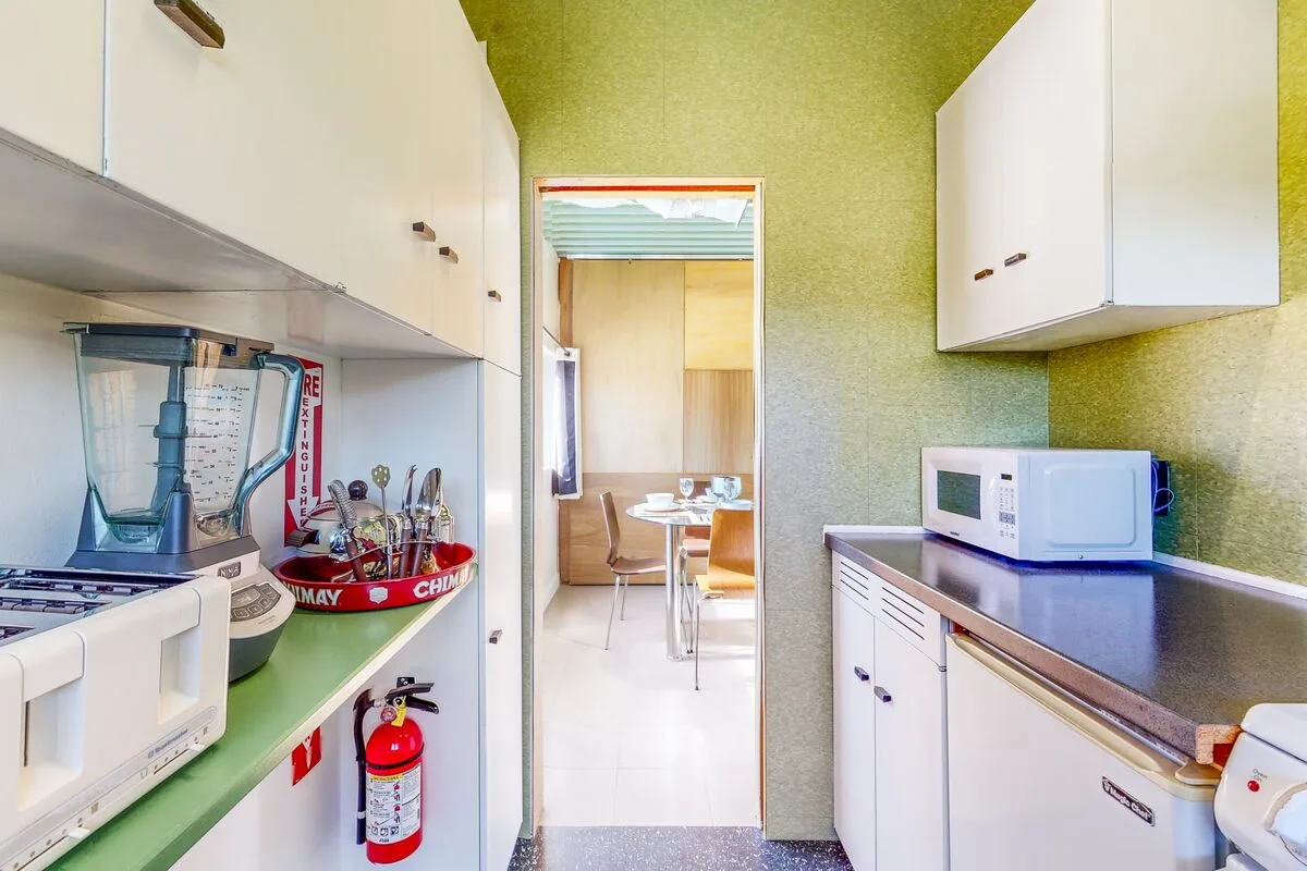 A narrow kitchen with counters and appliances opens into a dining area.