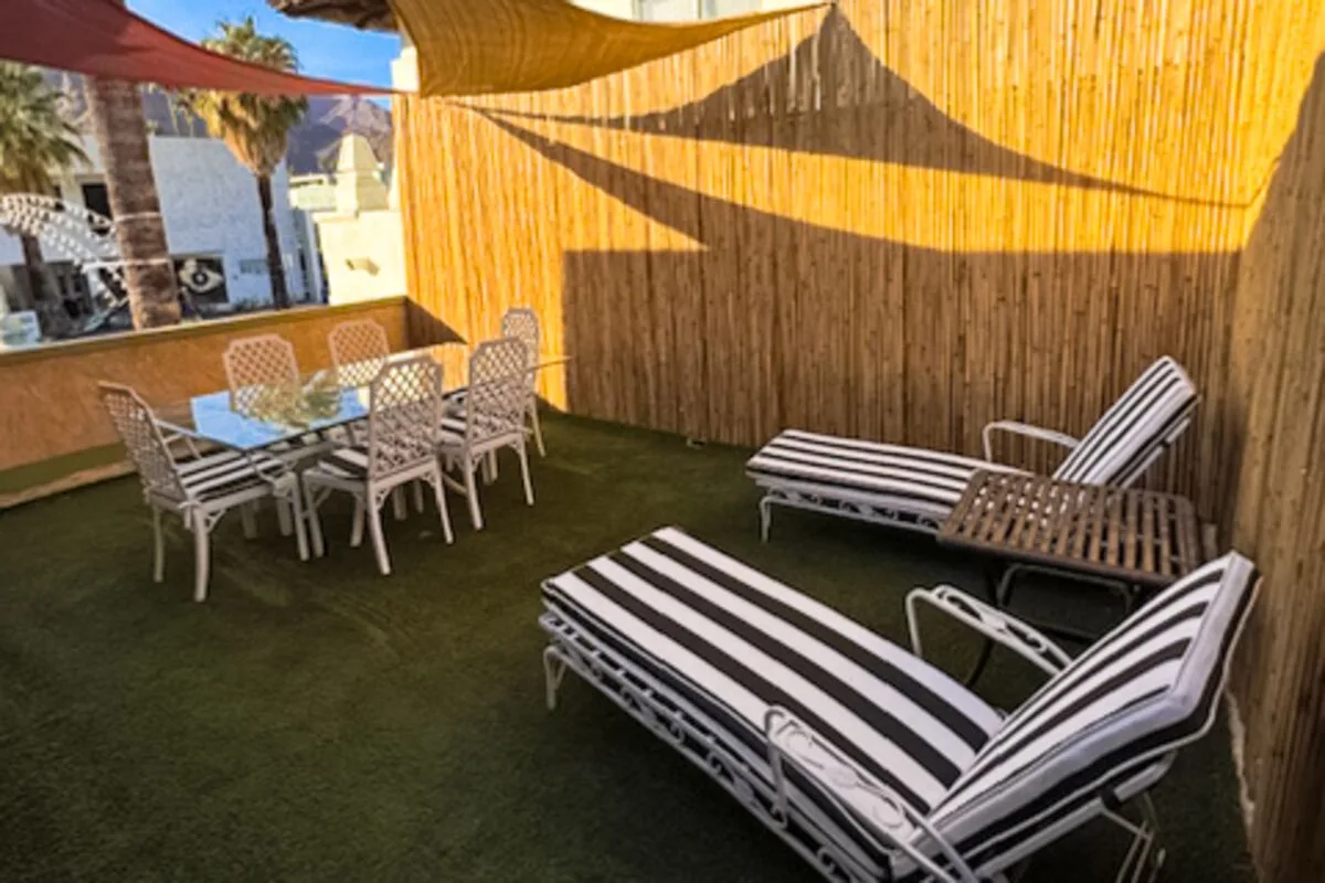 An outdoor patio has a dining table and striped lounge seating beside a reed fence.