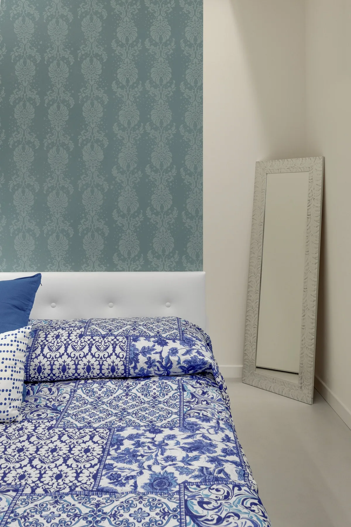 Un dormitorio con ropa de cama estampada azul y blanca y un espejo de cuerpo entero.