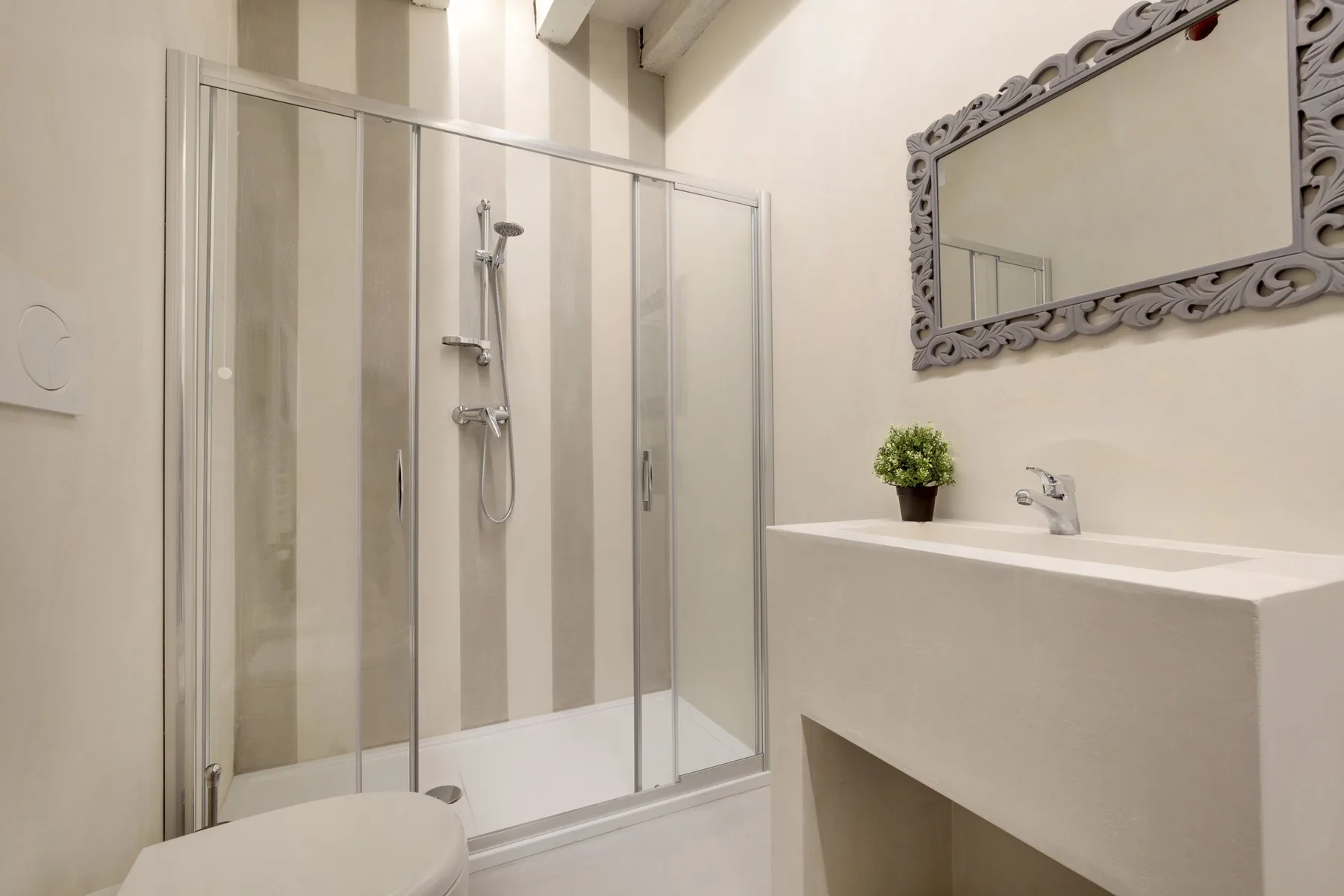 Un baño luminoso con ducha de vidrio y un lavabo blanco.