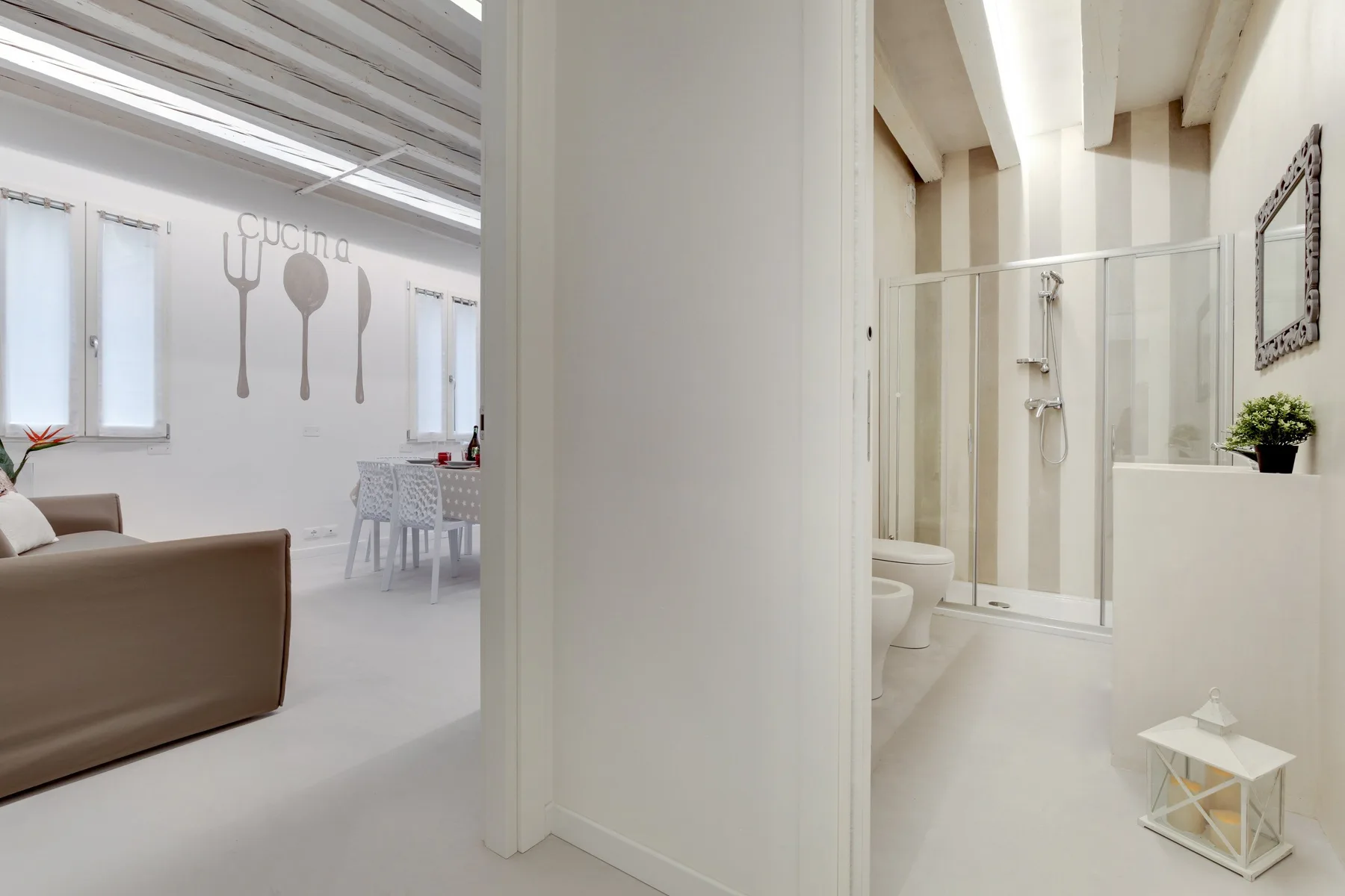 Un interior luminoso muestra una sala de estar y comedor junto a un baño con ducha de vidrio.