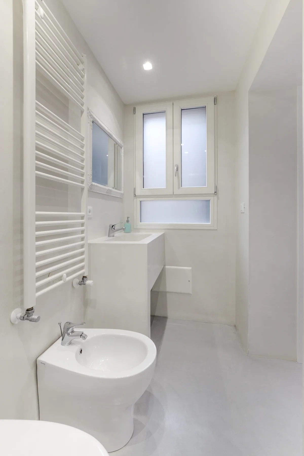 Un baño luminoso con lavabo, bidé y radiador toallero alto en la pared.