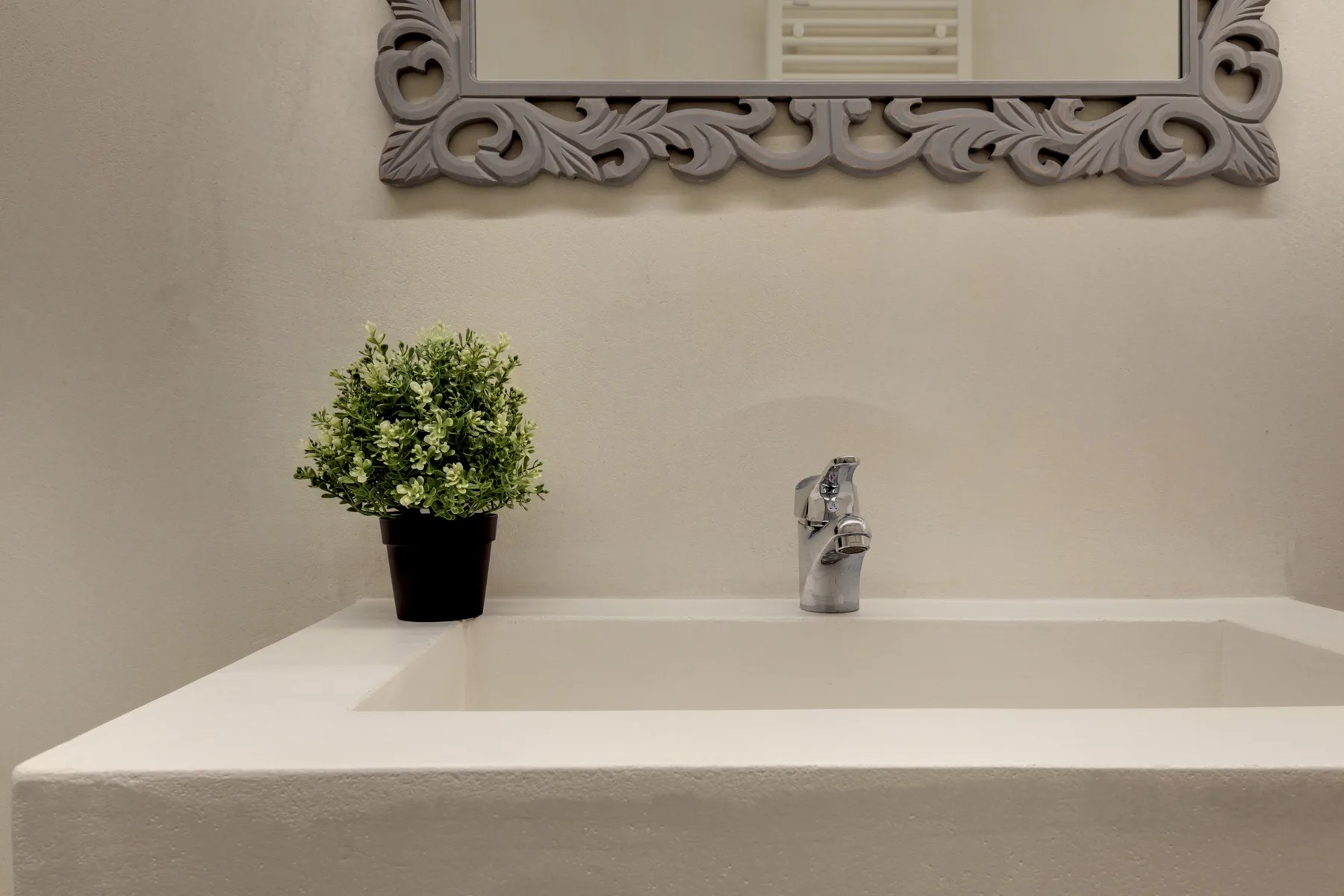 Un lavabo de baño con una pequeña planta en maceta y un espejo decorativo encima.