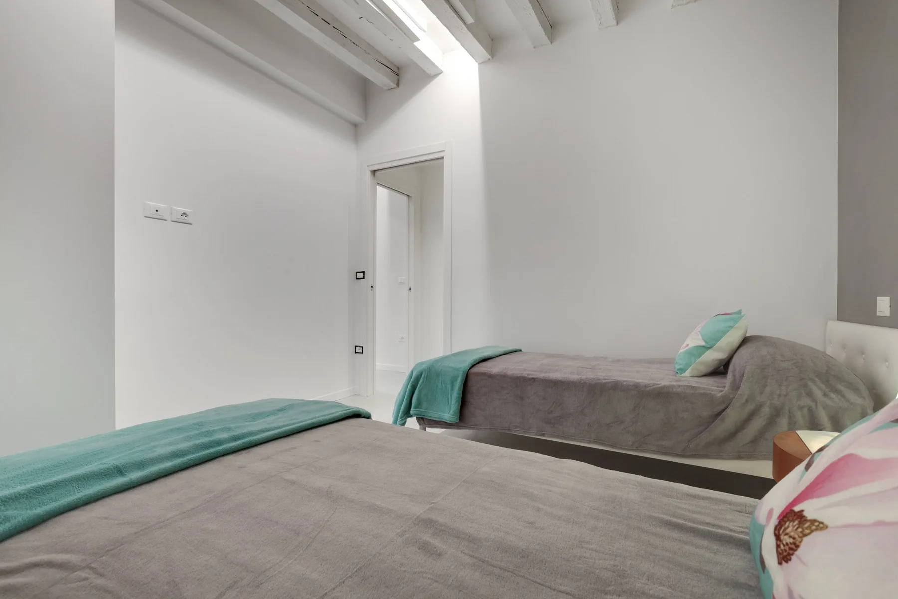 Un dormitorio con dos camas cubiertas de ropa de cama gris y detalles turquesa.