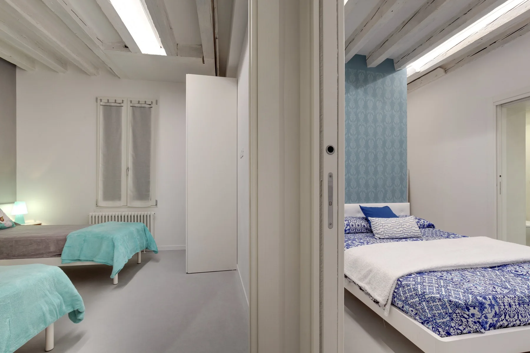 Un dormitorio con camas, ropa de cama turquesa y una pared decorativa azul estampada.