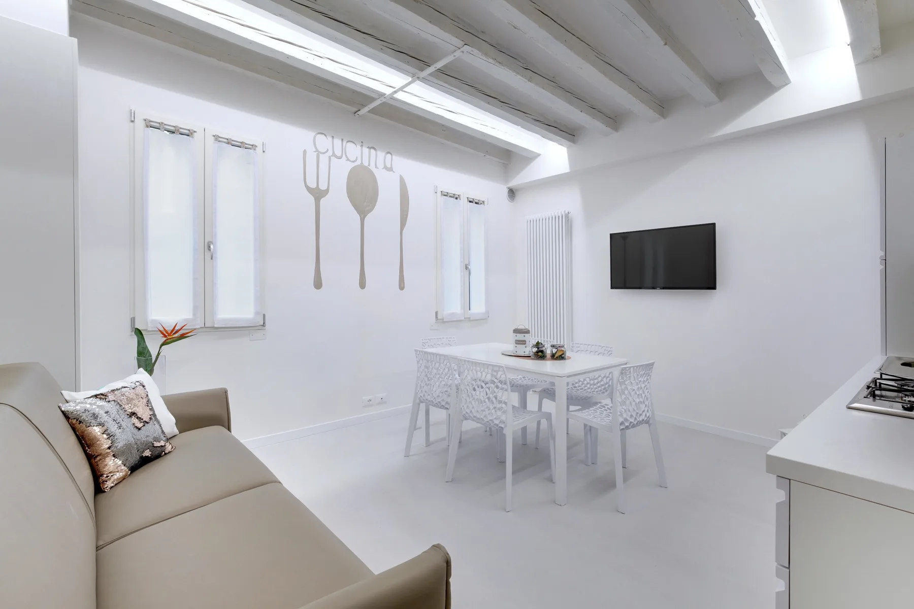 A bright white dining area has a table and seating beneath exposed ceiling beams.