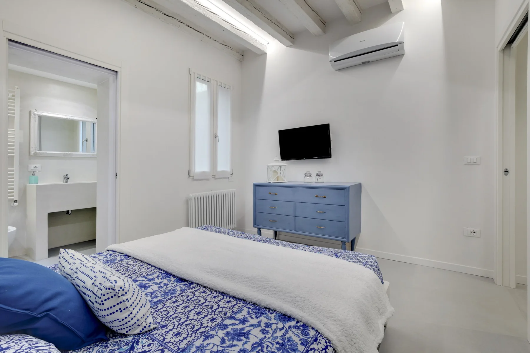 Un dormitorio con una cómoda azul, un televisor en la pared y una cama.
