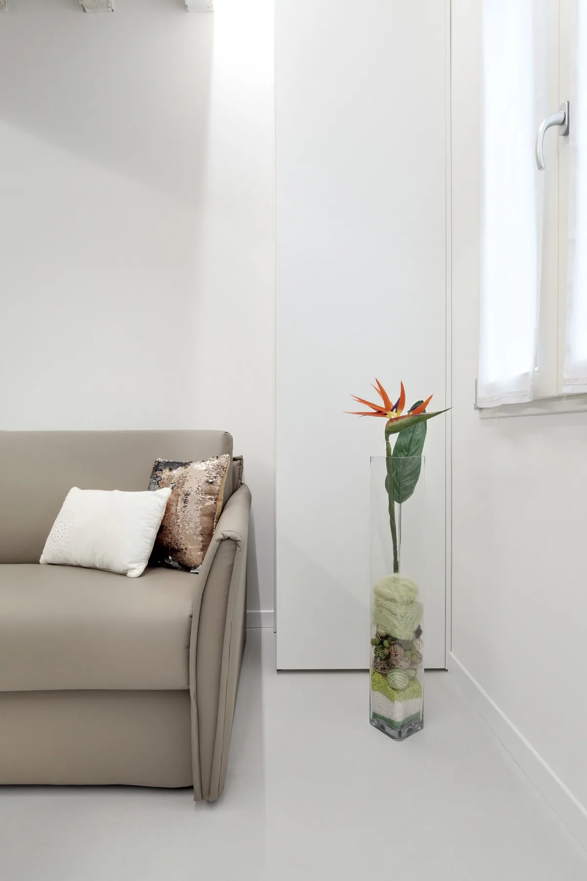 Una sala luminosa con un sofá neutro y un jarrón alto con flores.