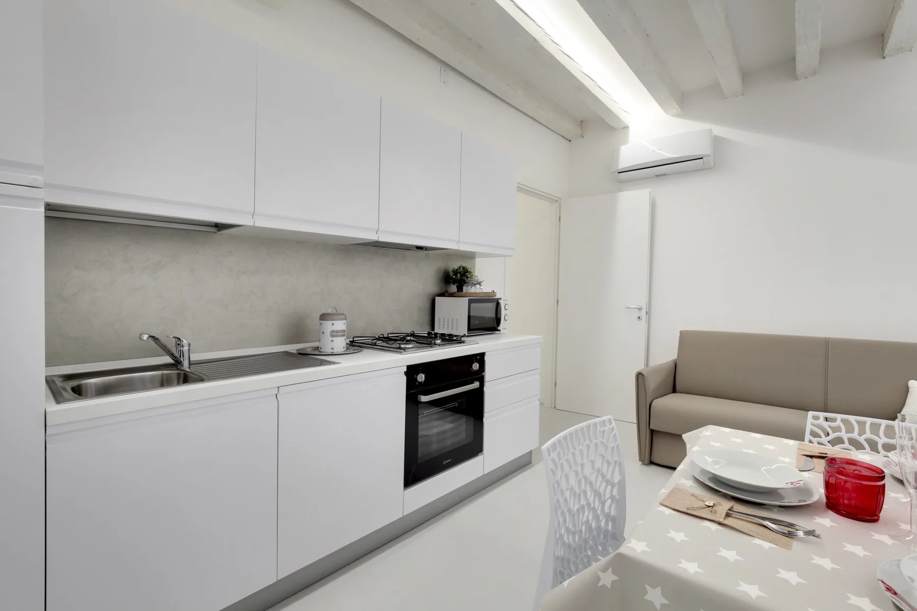 Una cocina y comedor luminosos con gabinetes blancos y una mesa puesta para comer.
