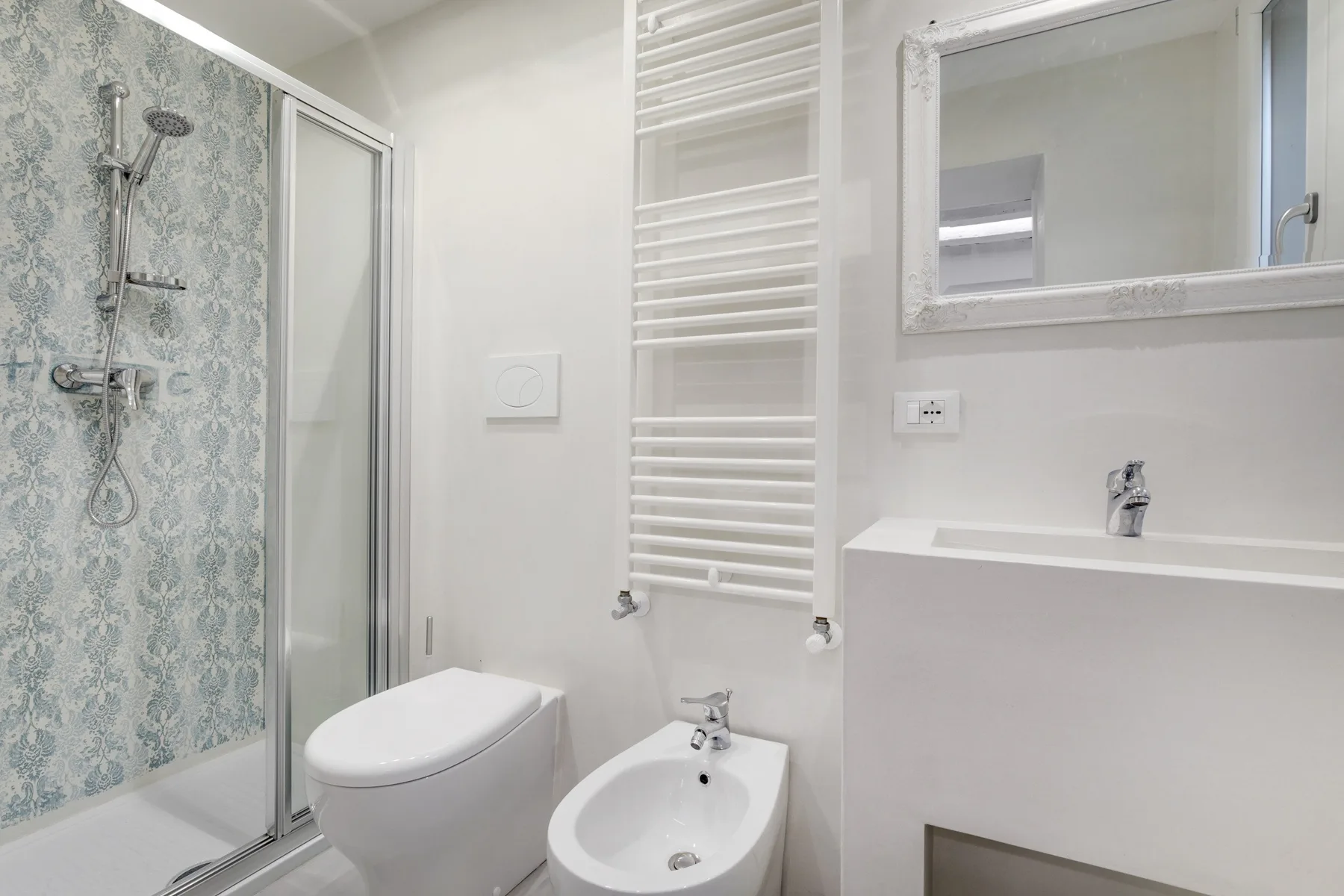 Un baño luminoso con una pared de ducha estampada y sanitarios blancos.