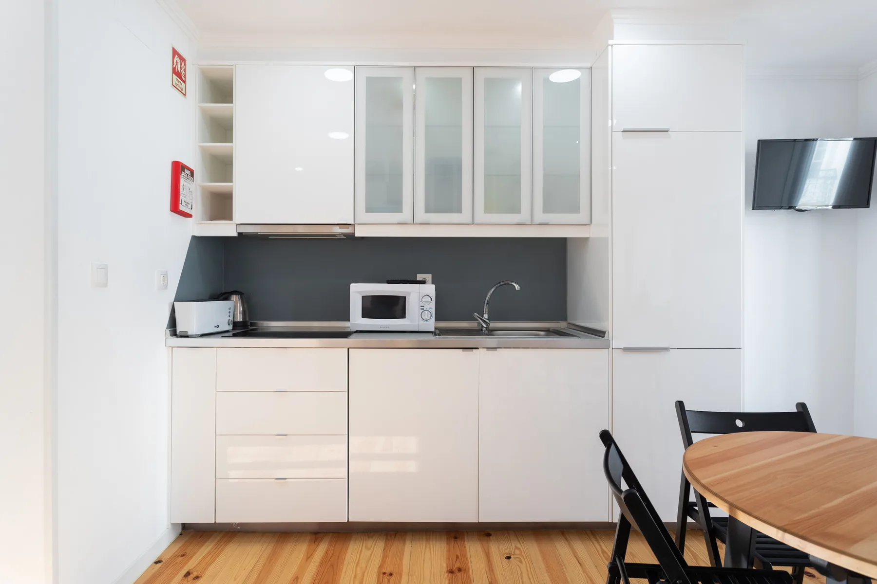 Una cocina compacta con armarios blancos, un salpicadero oscuro y una mesa de comedor de madera.