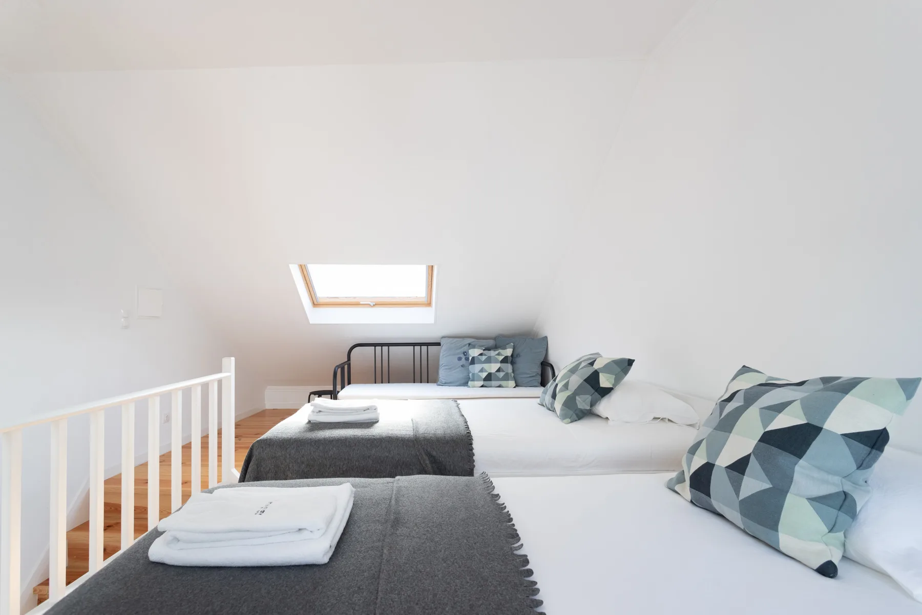 Un dormitorio abuhardillado luminoso con camas y cojines geométricos.