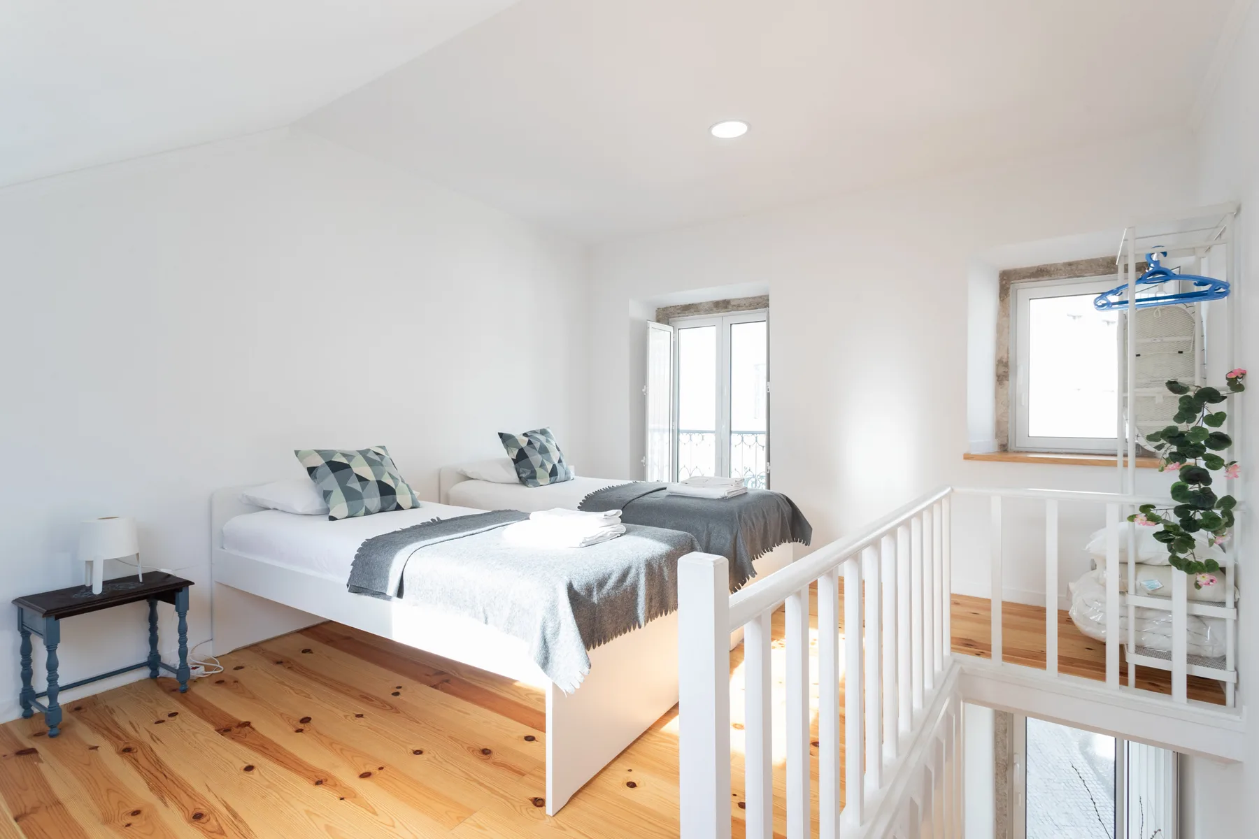 Un dormitorio luminoso con dos camas, suelo de madera y una barandilla blanca.