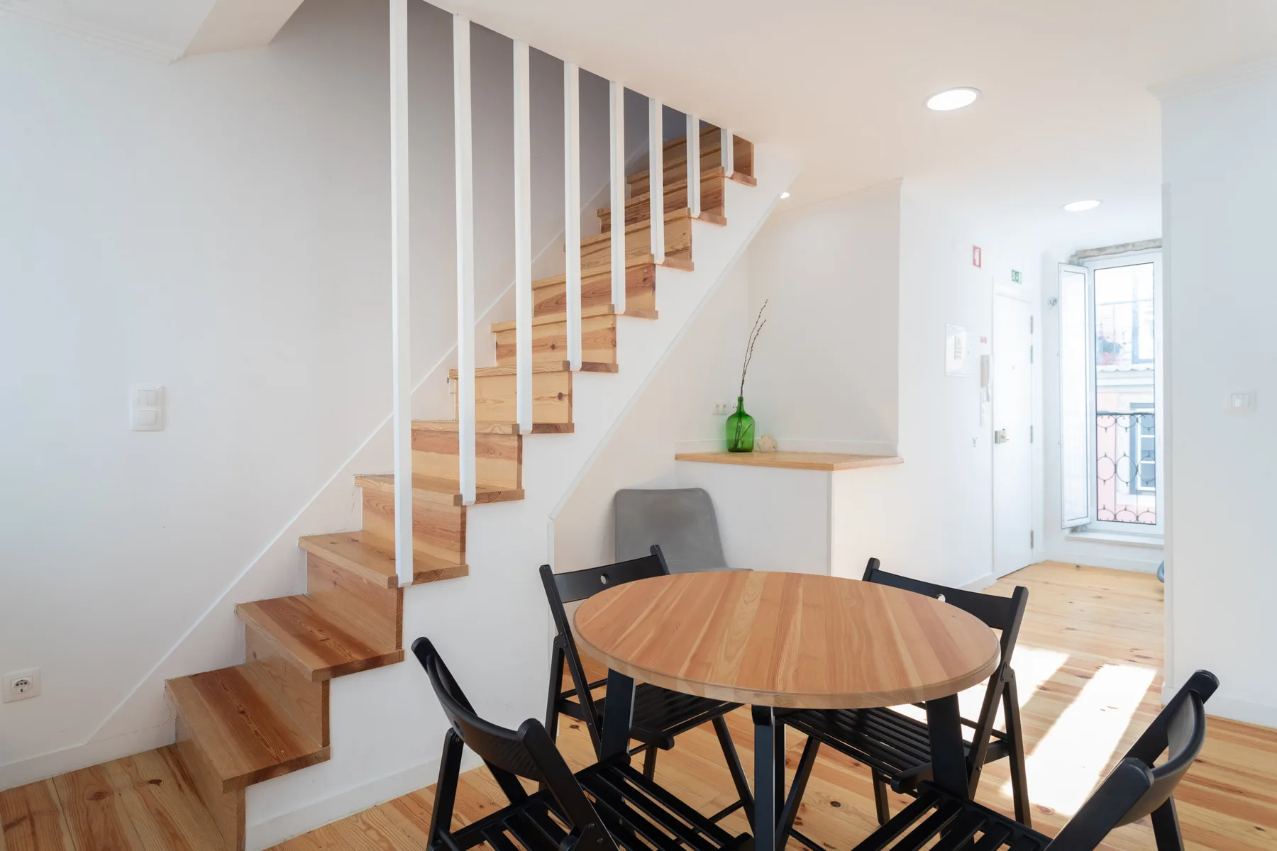 Un comedor con una mesa redonda de madera y una escalera junto a la pared.