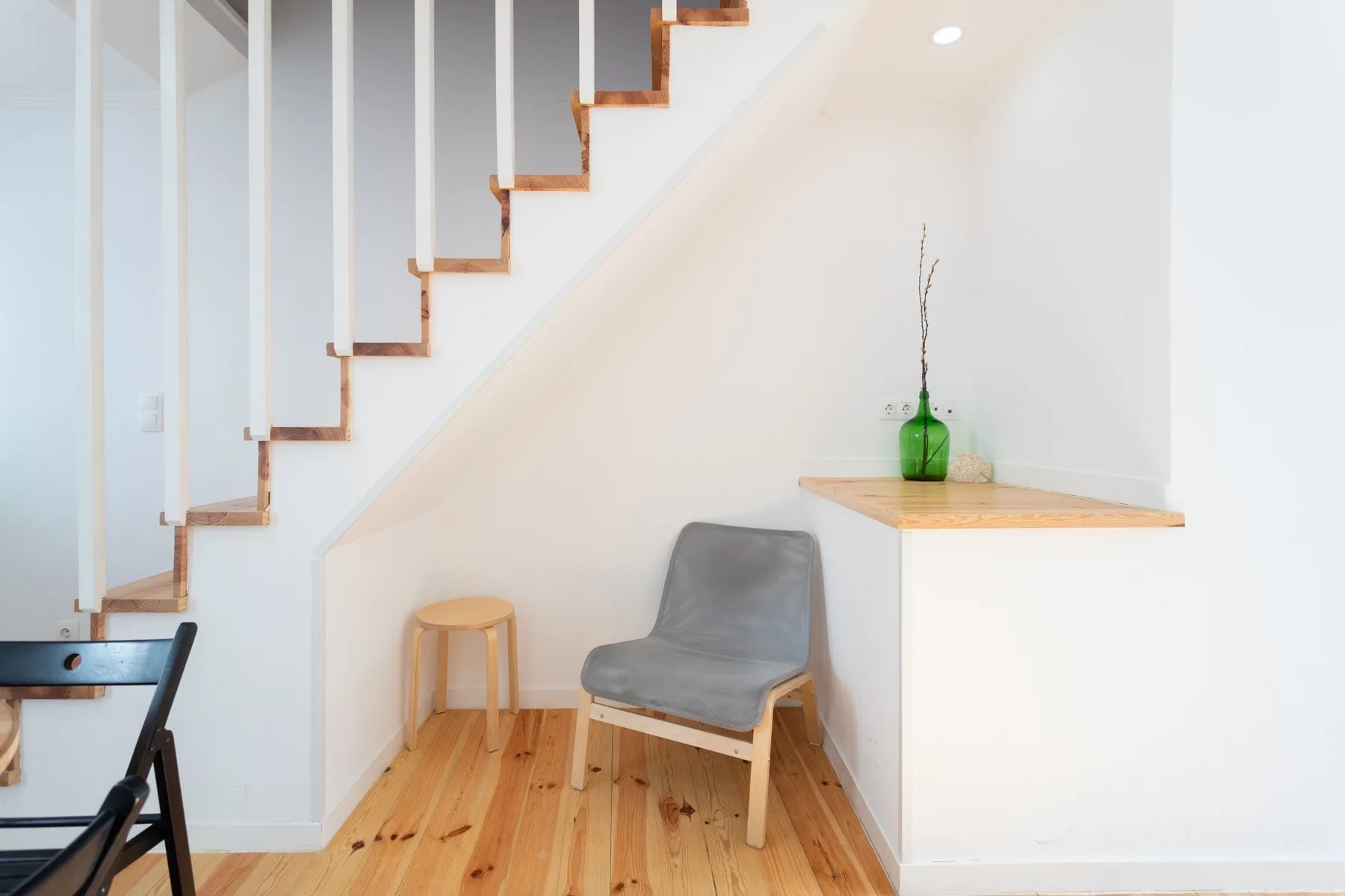 Un pequeño rincón para sentarse bajo una escalera, con una silla gris y un estante.