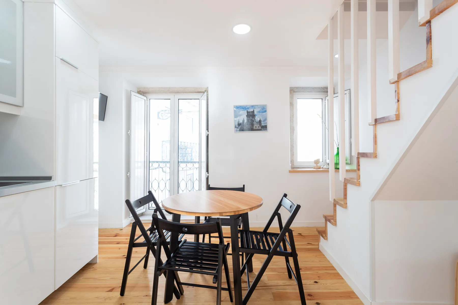 Una luminosa zona de comedor con una mesa de madera y asientos negros junto a una escalera.
