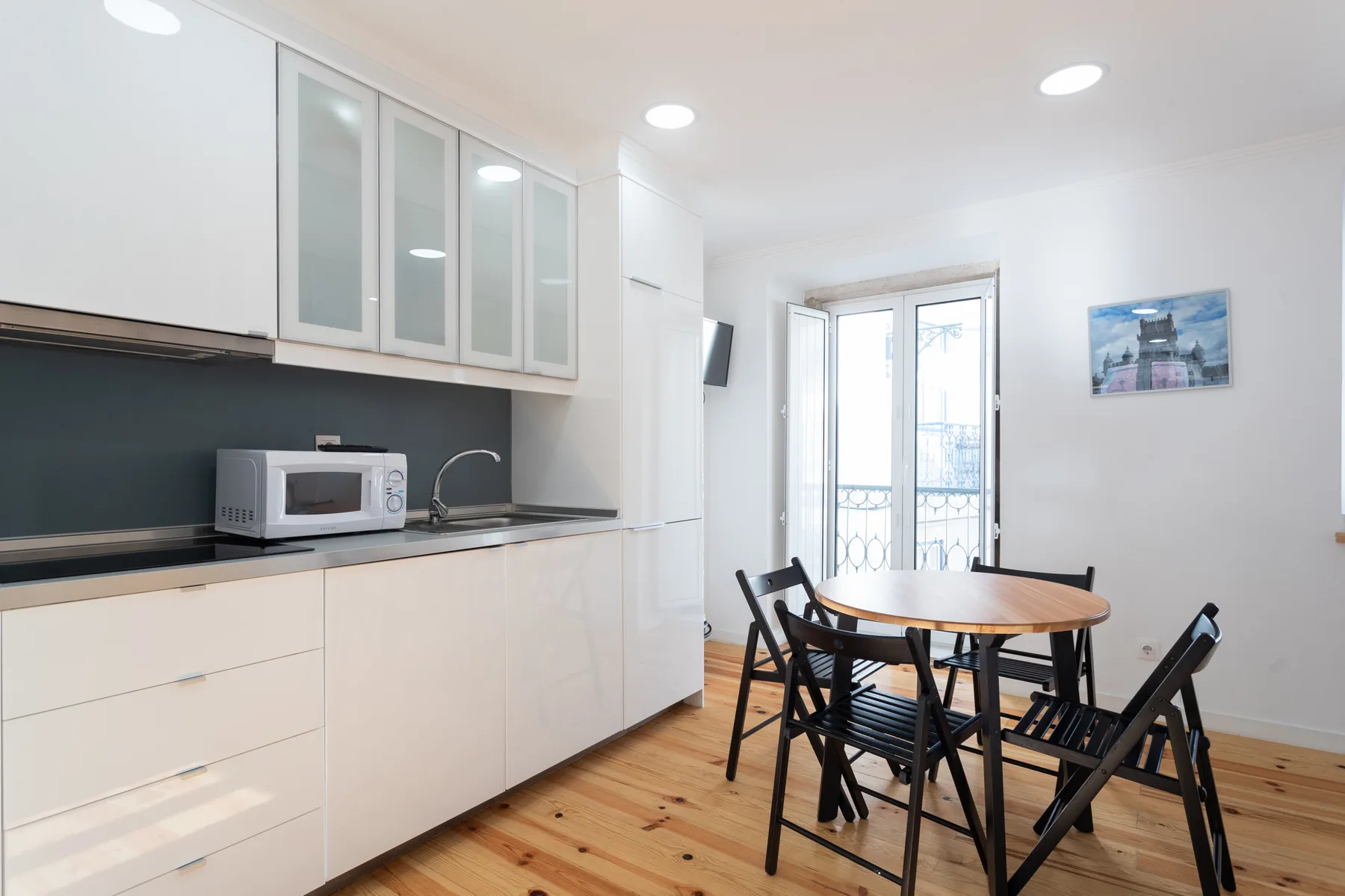 Una cocina y comedor luminosos con armarios blancos y una mesa de madera.