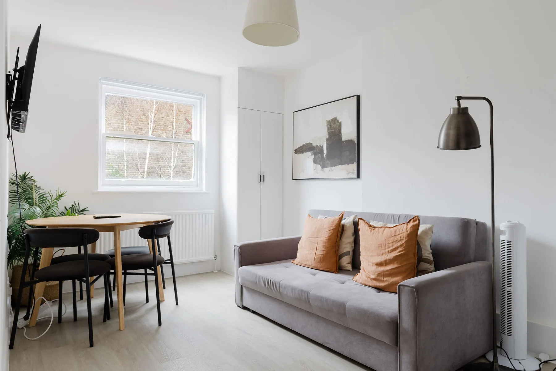 A bright living room with a gray sofa, dining table, and window.
