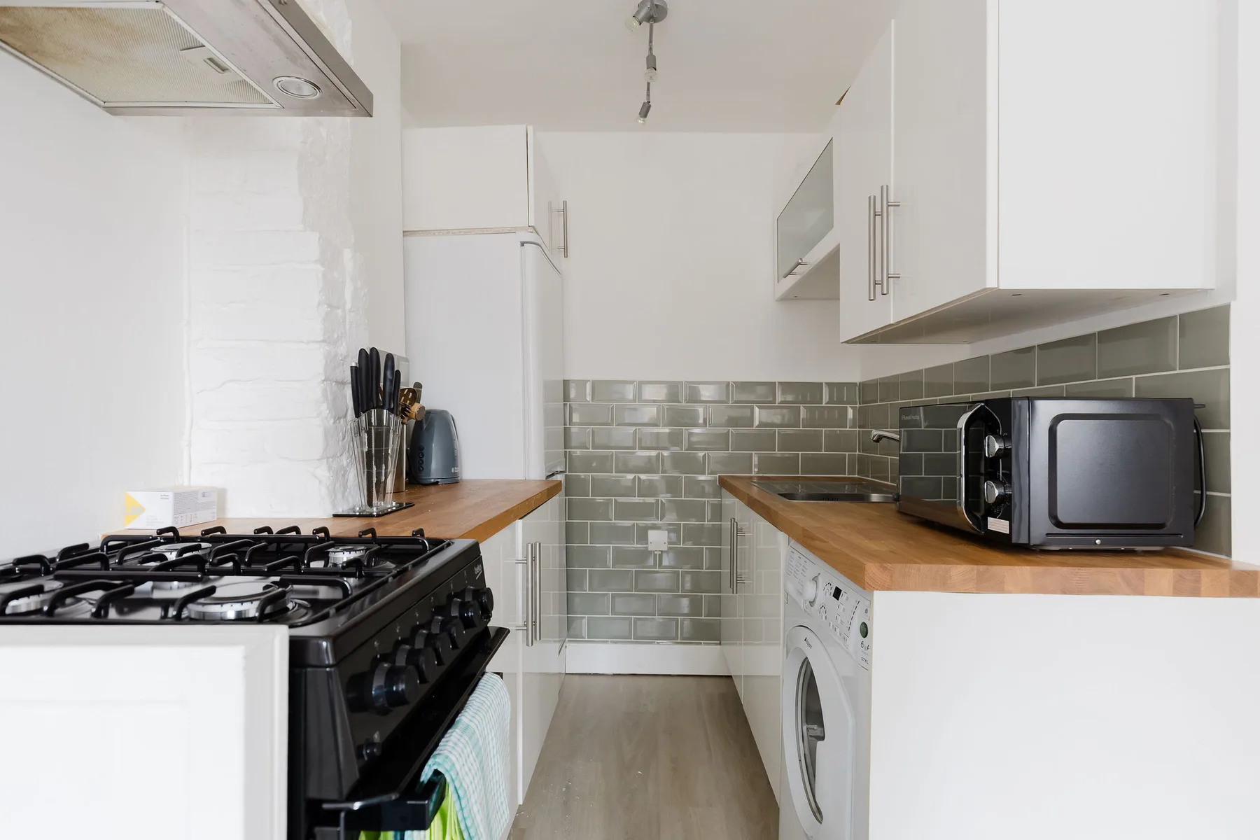 A compact kitchen with a gas range, wooden counters, and white cabinets.