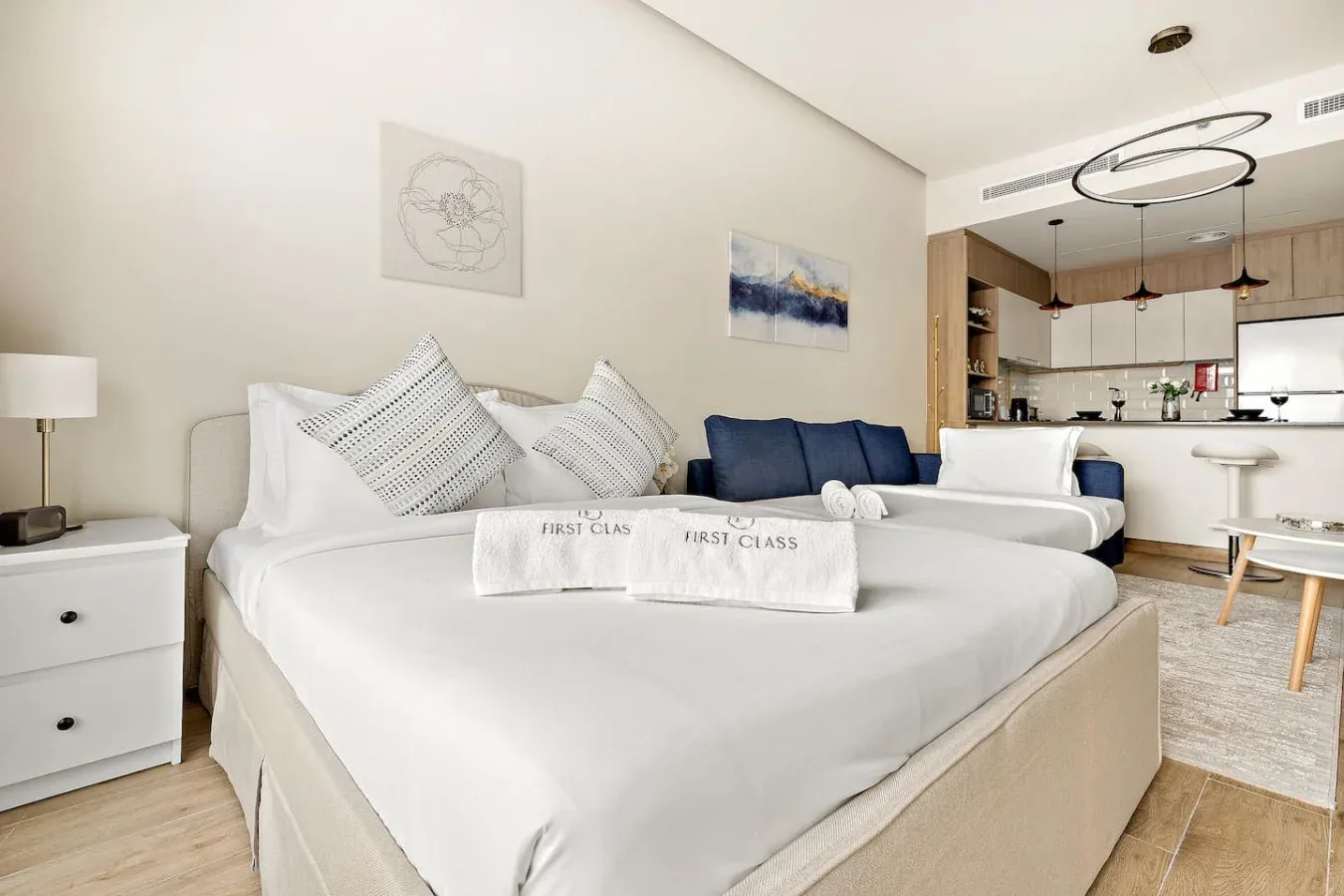 A bright bedroom with a large bed and a small kitchenette in the background.
