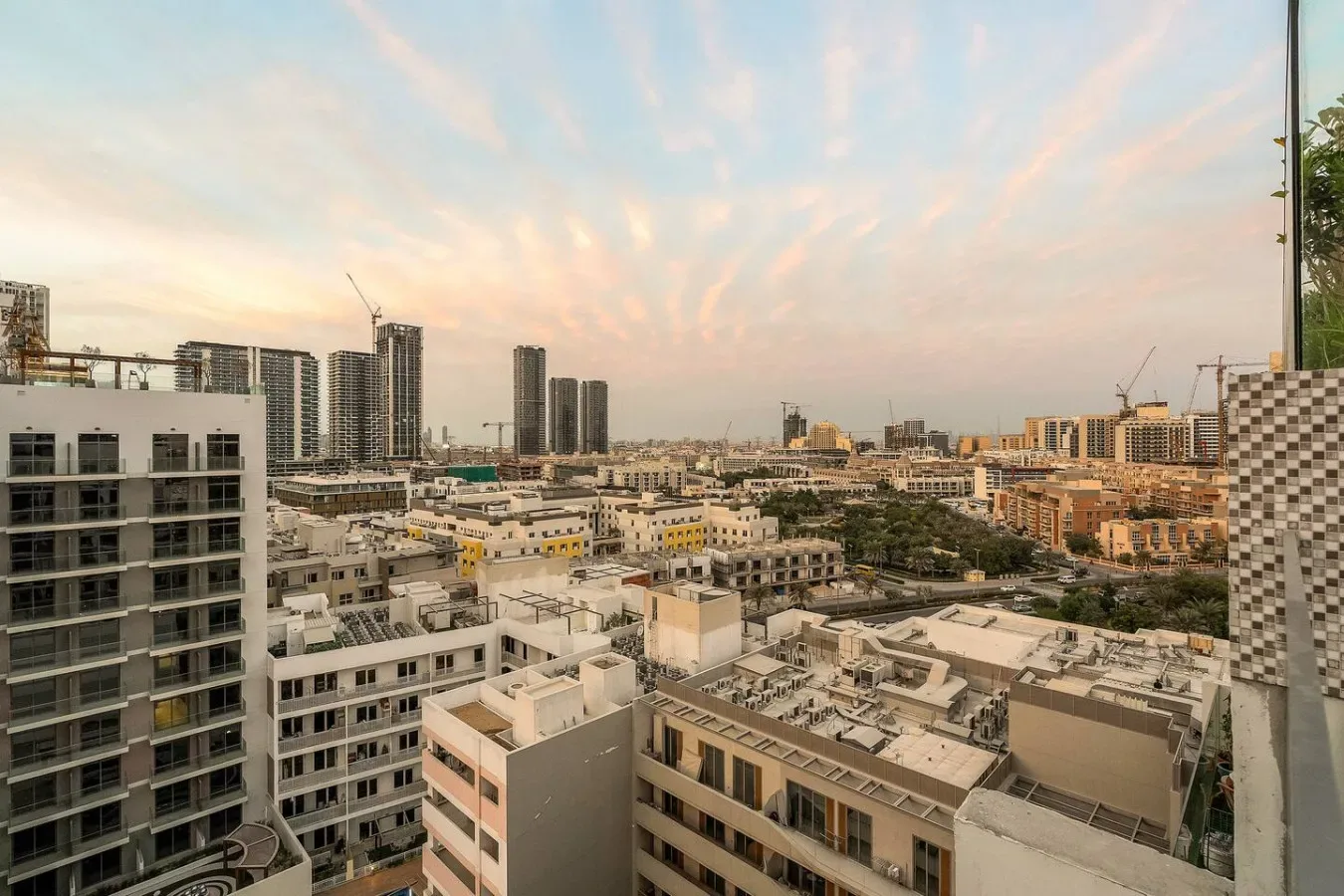 City skyline viewed above a dense cluster of mid-rise buildings beneath a pastel sky.