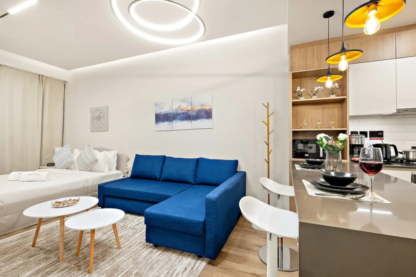 A bright living area with blue seating beside an open kitchen and dining counter.