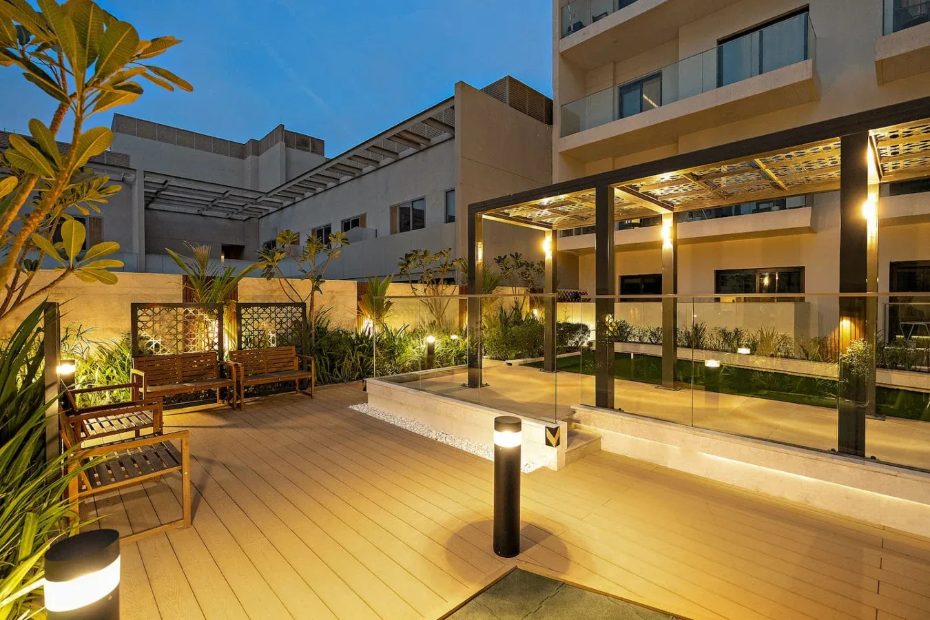 An outdoor patio with seating, plants, and a lit walkway beside a building.
