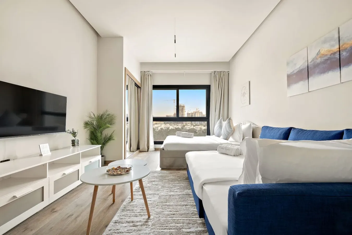 A bright living room with white seating, a television, and a large window.