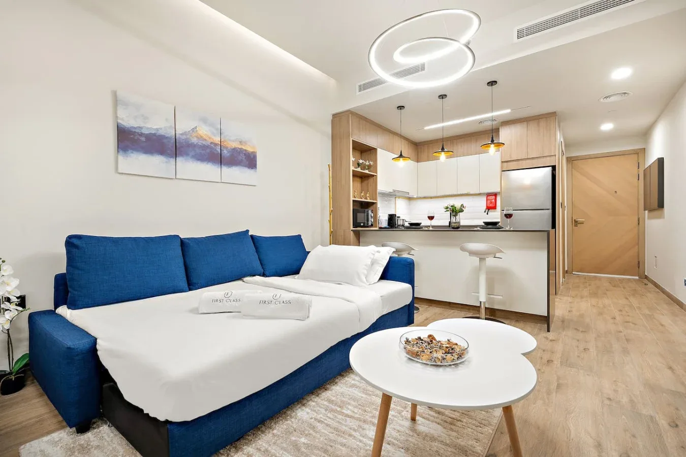 A bright living area with blue seating and a compact kitchen behind it.