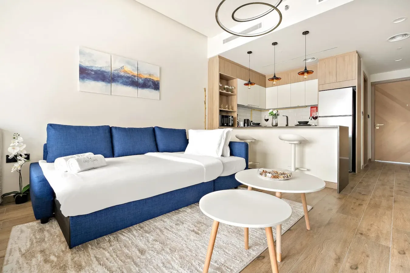 A bright living area with blue seating, a coffee table, and an open kitchen.