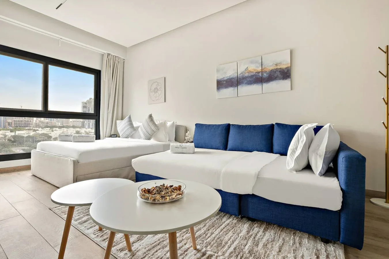 A bright living room with a blue sectional sofa, white tables, and large windows.